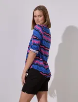 Camisa de manga 3/4 con estampado zig zag en tonos azul, rosa y negro. Tiene cuello con solapa, escote en V, abertura central con botones y bolsillo simulado en el pecho.