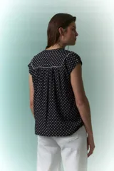Blusa negra con lunares blancos, escote en V y cuello bebé con borde blanco.