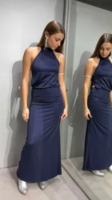 Vestido largo de fiesta color azul marino con acabado brillante. Presenta un diseño de cuello halter con frunces en el escote, espalda descubierta y detalle de frunces laterales en la cintura que realzan la silueta.