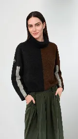 Polera de cuello alto confeccionada en lana lambswool, con diseño bicolor en negro y marrón. Presenta mangas largas con franjas verticales en gris y un parche circular bordado en la manga derecha.