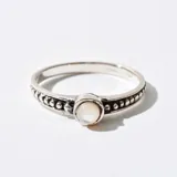 Anillo plateado con una piedra redonda blanca en el centro y detalles de pequeñas esferas en los bordes.