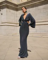 Vestido largo color verde esmeralda, con escote en V, corte a la cintura y falda con abertura lateral. Mangas largas acampanadas y espalda descubierta.