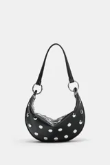 Bolso de mano tipo saca con diseño redondeado, confeccionado en material sintético color marrón oscuro. Presenta múltiples tachas metálicas doradas distribuidas por toda la superficie y un asa superior sujeta por anillas metálicas doradas. Cuenta con cierre superior mediante cremallera metálica.