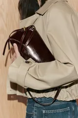 Bolso de hombro tipo baguette en color negro con acabado brillante. Presenta un diseño rectangular con cierre de cremallera superior y doble asa ajustable mediante hebillas metálicas.