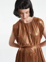 Mono largo sin mangas de corte holgado, confeccionado en tejido plisado con acabado metalizado. Presenta cuello redondo con detalle de abertura y cierre de botón en la parte posterior.