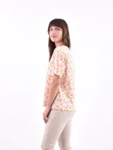 Remera de manga corta color beige con estampado de bananas en tonos amarillo, naranja y rosado.