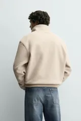 Sudadera de corte relajado confeccionada en tejido con textura de borreguillo, con cuello subido y cierre frontal de botones a presión. Presenta puños y ruedo con acabado en rib.