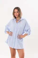 Vestido camisero de lino color celeste, con escote en V, cuello clásico, cierre frontal de botones y mangas tres cuartos regulables. Diseño holgado con corte asimétrico.