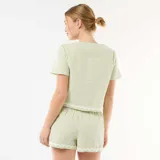 Pijama de dos piezas de cuadros vichy en tonos verde claro y blanco. Incluye una camisa de manga corta con escote en V y cierre frontal mediante lazos, y un short con cintura elástica y cordón ajustable. Ambas prendas cuentan con detalles de ondas bordadas en los bordes.