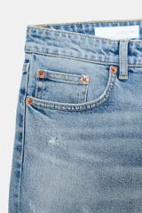 Jeans de denim azul oscuro con efecto desgastado y lavado, tiro bajo, corte bootcut y bajo flare. Presenta cinco bolsillos y cierre frontal con cremallera y botón.