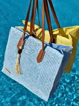 Bolso de playa amarillo tejido con asas de cuero marrón y detalle de borla con cuentas. Interior forrado con tela celeste.