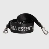 Correa para cartera de cinta tejida negra con la inscripción 'BUBBA ESSENTIAL' en color plateado. Cuenta con ganchos metálicos en los extremos y detalles en cuero sintético.