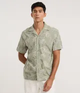 Camisa de manga corta color verde militar, con cuello solapa, cierre frontal de botones y diseño bordado de hojas. Modelo comfort de corte holgado.