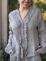 Camisa de lino color gris claro, de manga larga y corte holgado, con cuello mao y detalle de volados en el frente a lo largo de la botonera.