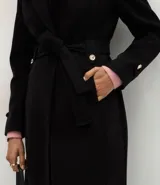Saco femenino de corte midi confeccionado en polyvelour, con diseño cruzado, cuello tipo blazer, mangas largas con detalles en puños, cierre frontal con lazo ajustable en la cintura y botones metalizados decorativos.