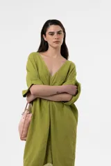 Vestido midi de lino color marrón, de corte amplio y silueta asimétrica con escote en V y detalle fruncido en el centro del frente. Presenta mangas cortas holgadas con vuelta y diseño relajado.