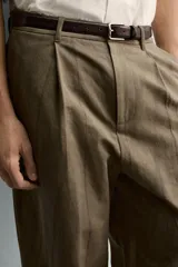 Pantalón de corte relajado confeccionado en mezcla de algodón y lino, con diseño de pliegues frontales, bolsillos laterales y bolsillos traseros de vivo. Presenta cierre frontal con cremallera y botón, con un acabado de lavado especial que le otorga una apariencia única.