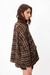 Chaqueta de corte holgado con estampado de cuadros en tonos marrones, blancos y negros. Presenta cuello de pana en color marrón oscuro, cierre frontal con botones metálicos y bolsillos laterales amplios.