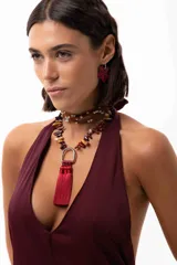 Collar corto con cadena de piedras naturales en tonos tierra y un dije central metálico en forma de herradura del que cuelgan tres borlas de seda en color bordó.