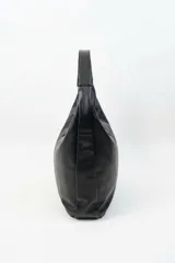 Bolso tipo hobo de cuero sintético negro, con cierre superior y correa de hombro integrada. Incluye un llavero colgante metálico con forma de perrito inflable.