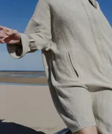 Tapado amplio color gris claro, confeccionado en lana fina sin teñir. Tiene hombros caídos, mangas largas con presillas y detalle de color en el cuello.