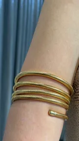 Brazalete rígido de diseño en espiral tipo serpiente, con acabado metálico dorado y textura acanalada.
