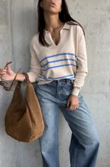 Sweater de punto fino color beige, con cuello polo y escote en V. Presenta tres rayas horizontales azules en el pecho y mangas largas con puños acanalados.