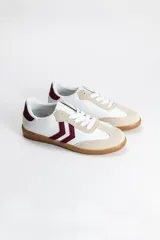 Zapatilla de estilo urbano con diseño acordonado, confeccionada en una combinación de cuero sintético blanco, detalles en gamuza beige y apliques laterales en color bordó. Cuenta con suela de goma tipo caramelo.