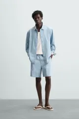 Shorts de denim de algodón, color celeste lavado, de corte regular fit y largo hasta la rodilla. Presenta cierre frontal con cremallera y botón, bolsillos delanteros y bolsillos traseros de plastrón. El borde inferior tiene un acabado deshilachado.