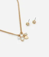 Conjunto de bisutería en tono dorado que incluye un collar con cadena de eslabones y dijes colgantes de perla sintética, corazón y cristal, junto con un par de aros tipo caravana con diseño de nudo y cristal.