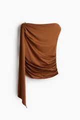 Top color marrón de punto elástico, con un hombro descubierto y una tira larga que cae desde el hombro. Presenta fruncidos en los laterales para un efecto drapeado.