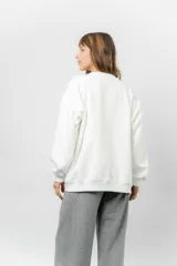 Buzo oversize de algodón frizado color beige, con cuello redondo, puños y cintura tejidos. Presenta un bordado pequeño de Snoopy en el frente.