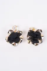 Caravanas colgantes con diseño de flor, combinando pétalos de tela negra y pétalos metálicos dorados, con un cristal transparente en la parte superior.