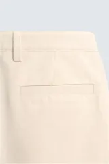 Pantalón chino de algodón color beige, de corte relajado (relaxed fit) y tiro medio. Presenta bolsillos delanteros y bolsillos traseros de vivo con cierre de cremallera y botón.