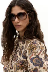 Camisa de algodón con estampado paisley en tonos beige, azul y naranja. Presenta cuello mao, hombros abullonados, mangas largas con puño elástico y botones de nácar en el frente con un detalle de vuelo.