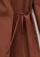 Camisa de algodón color marrón, de diseño cruzado estilo sobre con lazo lateral para anudar, cuello camisero, manga larga y calce amplio.