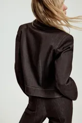 Chaqueta corta de denim oscuro con cuello solapa, cierre frontal con cremallera y bolsillos delanteros de plastrón con solapa. Presenta mangas largas con hombreras y costuras a la vista.