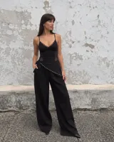 Pantalón negro de tiro alto y corte amplio con bolsillos laterales, que cuenta con una tira cruzada decorada con tachas metálicas en la parte frontal.