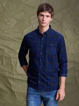 Camisa de manga larga con diseño a cuadros en tonos azul marino, verde y líneas rojas. Presenta cuello clásico, cierre frontal con botones y dos bolsillos con solapa en el pecho.