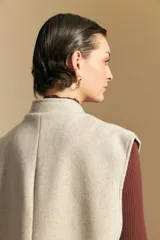 Chaleco de paño color marrón oscuro, de silueta recta y diseño minimalista. Presenta cuello a la base, cierre frontal con botones claros y bolsillos aplicados.
