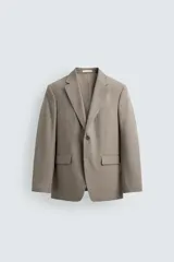 Blazer slim fit de color beige, confeccionada en tejido con lana. Presenta cuello con solapas de muesca, cierre frontal de un botón, bolsillos laterales con solapa y bolsillo de vivo en el pecho.