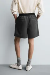 Bermuda de corte relajado color gris oscuro jaspeado, con cintura elástica negra ajustable mediante cordón negro. Presenta bolsillos frontales y bolsillos traseros de vivo.