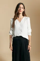 Camisa negra de manga larga con escote en V y cierre frontal de botones. Presenta detalles de volados en los hombros, frunces en la espalda y puños elastizados que le otorgan una silueta relajada y fluida.