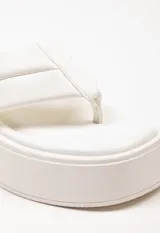 Sandalia tipo ojota con plataforma, confeccionada en material sintético color blanco. Presenta una tira ancha acolchada con detalle de costura central y diseño de separación para el dedo.
