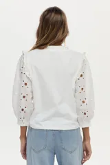 Blusa blanca con mangas abullonadas de broderie, cuello elevado con volados y detalles de volados en los hombros.