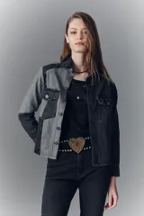 Campera de denim rígido con diseño de recortes en tonos gris y negro. Presenta cuello camisero, cierre frontal con botones metálicos, bolsillos con solapa en el pecho y corte recto.