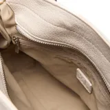 Cartera chica tipo morral color beige, confeccionada en símil cuero, con doble asa de mano y correa larga ajustable y desmontable. Cuenta con detalles de cordones laterales y herrajes metálicos plateados con el logo de la marca.