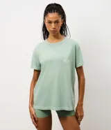 Remera de algodón con calce oversized, cuello redondo y mangas cortas. Presenta un diseño minimalista con un pequeño estampado de texto en el pecho y un acabado lavado en color verde menta.