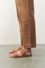 Sandalias planas de símil cuero marrón, con dos tiras anchas adornadas con apliques metálicos dorados.