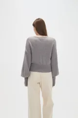 Saco de punto color beige, con cuello redondo, cierre frontal con botones y mangas largas con puños acanalados.